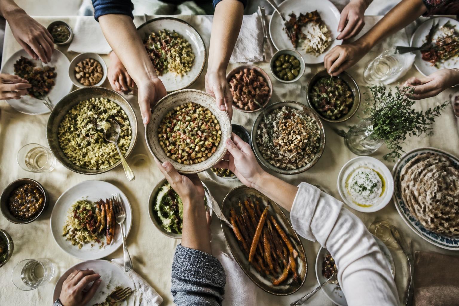 Overhead view of many hands passing vegetarian dishes around a shared table